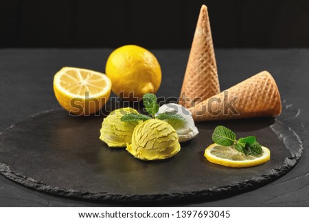 Tasty creamy and lemon ice cream decorated with mint served on a stone slate over a black background.