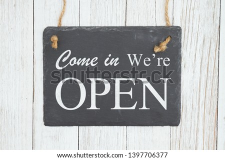 Advertise you are open with an retro sign, Come in we're Open text on a hanging chalkboard on weathered whitewash textured wood