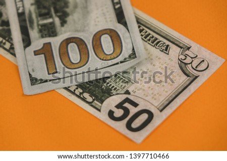 fifty and one hundred dollars lying on an orange background close up.