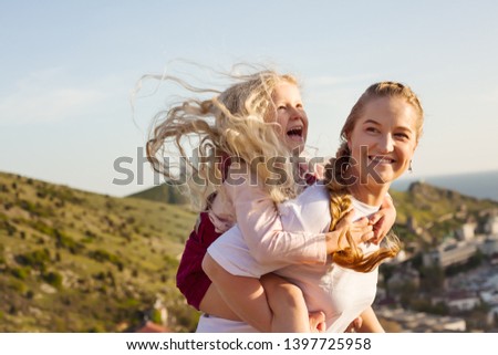 happy mother holding little blond daughter on hands  outdoors lifestyle against the bay and the old city.