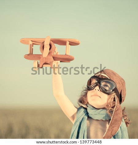Happy kid playing with toy airplane against blue summer sky background. Royalty-Free Stock Photo #139773448