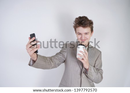 funny emotional teen boy standing with paper cup of tea and doing selfie on white background alone