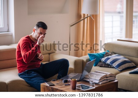 Tired student typing on his laptop and reading a book while sitting on a couch, showing a gesture with hand as ok, right, go for it sign