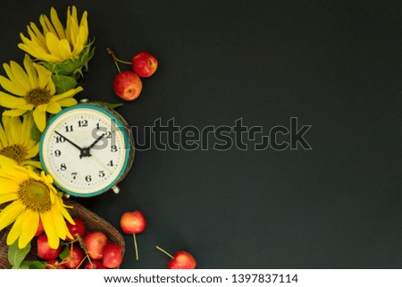 Old alarm clock near a bouquet of yellow sunflowers and flowers and red apples in a basket on a black background. Mother's Day or women. Greeting card Good morning, day. Copy space. The concept of