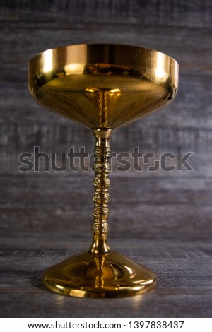 Golden glass on a table with a wooden brown background. Holy grail of cups.