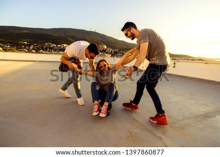 Teenage skateboards having fun while girl sitting on skateboard on the terrace at sunset