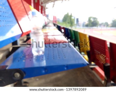 Blurred background of view of stadium with empty seat. Colorful seat in soccer stadium when holiday. Blue, green, red and yellow iron seats. Landscape of free arena seating.  