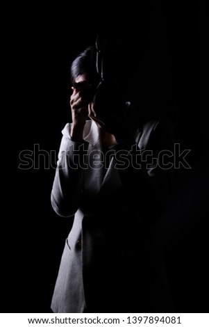Asian Woman Photographer hold camera with external flash point to shoot subject, wear gray suit. studio lighting black background isolated low key exposure, reporter journalist take photo celebrity