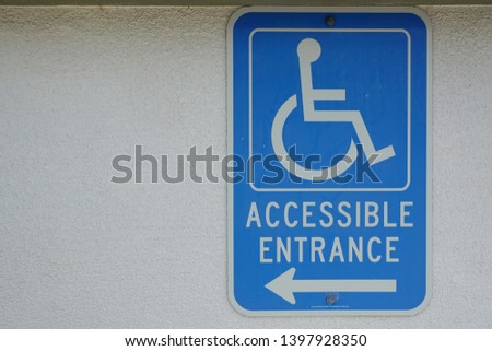 A blue sign on the wall with an arrow indicating the direction of the entrance ramp for disabled access.                          