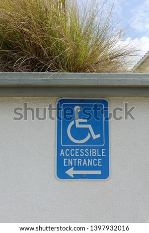 A blue sign on the wall with an arrow indicating the direction of the ramp for disabled access.