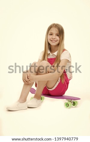 Small girl sit on skate board isolated on white. Child skater smile with longboard. Skateboard kid in pink jumpsuit. Sport activity and energy. Childhood and active games. Beauty on skateboard