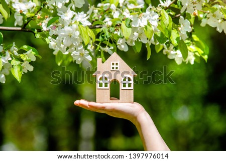 The girl holds the house symbol against the background of blossoming appletree  Royalty-Free Stock Photo #1397976014