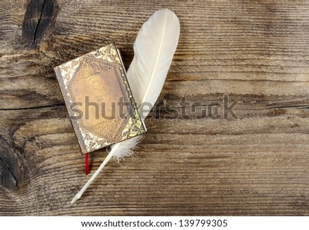 Book and feather on wooden rough background. Copy space.
