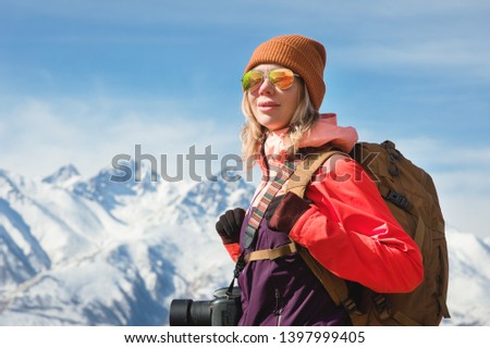 Portrait of photographer hipster tourist girl with a camera in sunglasses and a hat against the background of snow-covered Caucasus mountains. Photo travel concept