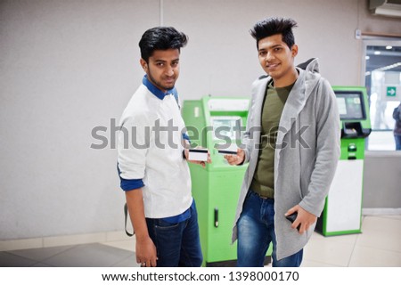 Two asian guys holding credit cards in hand against green ATM.