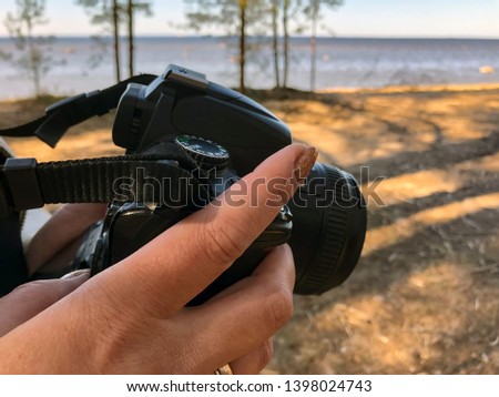 Reflex camera with swivel display in female hands on the background of a sandy seashore
