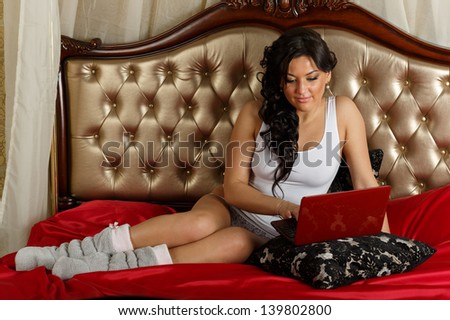 Young woman with laptop sits on the house bed.