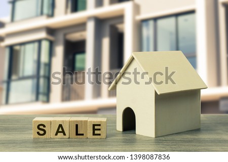 Home and real estate sale concept. A small residential model with sale wooden block on wood table on blurred real estate as background. Depicts house or residential project for rent or sale.