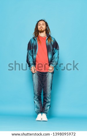 Cute man with dreadlocks in a pink T-shirt and in a fashionable suit and sneakers on a blue background in full growth                            