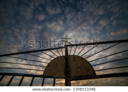 Iron gate with a cross on the background of a cloudy sky.