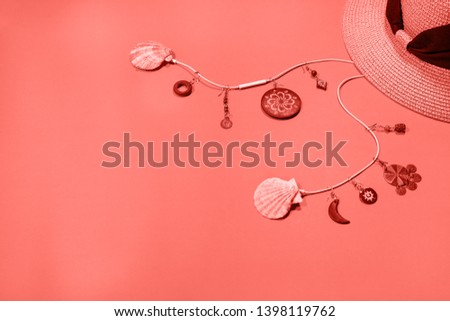 Earrings hanging from headphones with seashell speakers and straw hat on coral colored background