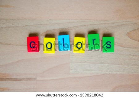 Toy lettering block in different colors on a wooden background that reads the word colors