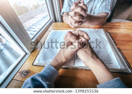 Two christian sitting around wooden table with praying to God together on holy Bible.
