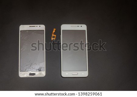 Smartphone after repairing a cracked touch screen. Nearby is a cracked touch screen. Black background with copy space.