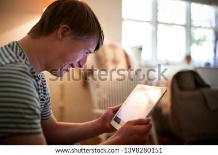 Young Downs Syndrome Man Sitting On Sofa Using Digital Tablet At Home Royalty-Free Stock Photo #1398280151