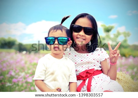 The girl and the boy wear sunglasses and sit with a finger to show the symbol in the Cosmos garden with the sky as the background. Close up. Selective focus.