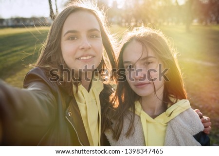 Two happy teenage friends taking selfie with mobile phone while walking in the park