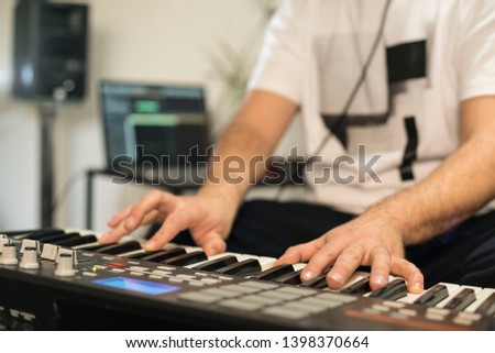Close up of professional musician recording midi keyboard in digital studio at home. He is surrounded with instruments and midi controller. Music production concept.