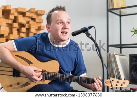 Professional musician recording electric guitar in digital studio at home. He is singing and surrounded with instruments and midi controller. Music production concept.