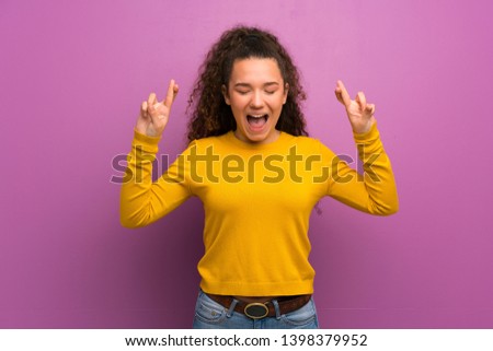 Teenager girl over purple wall with fingers crossing