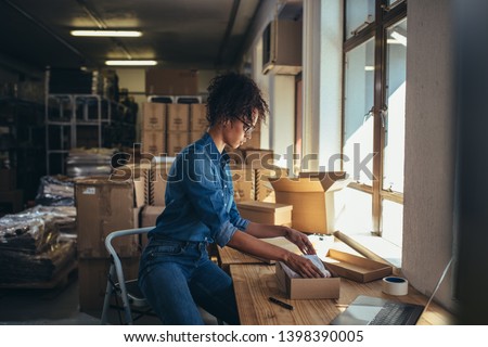 Female business owner working, packing the order for shipping to customer. Female entrepreneur packaging box for delivery. Royalty-Free Stock Photo #1398390005