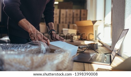 Small business owner packing in the cardbox at workplace. Cropped shot of man preparing a parcel for delivery at online selling business office. Royalty-Free Stock Photo #1398390008