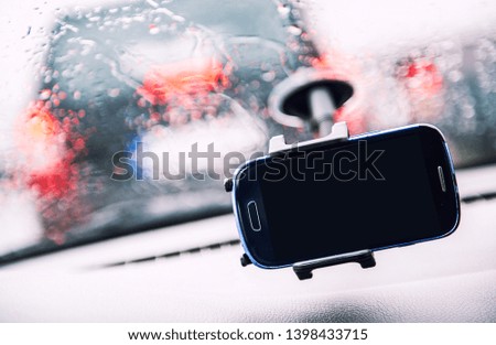 Smart phone on holder, rainy weather seen through wind shield, cellphone with black mock up blank on screen. Advertisement for traffic and navigation GPS apps concept close up image, no people