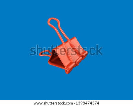 Large binder clip dipped in red paint and put against a blue background