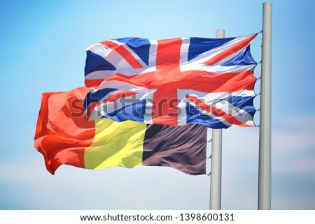 Flags of UK and Belgium against the background of the blue sky Royalty-Free Stock Photo #1398600131