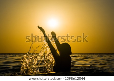 Girl swimming in the sea at sunset, splashes of transparency water, female black silhouette