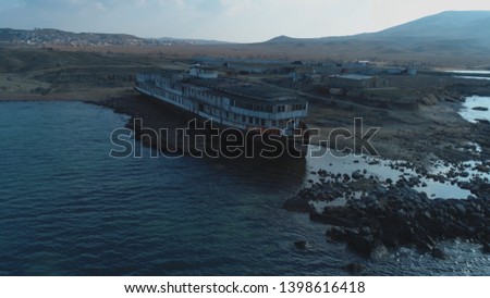 Od white and black large ship standing on the the pier near the sea water against the mountain hills and blue sky. Shot. Abandoned seagoing vessels Royalty-Free Stock Photo #1398616418