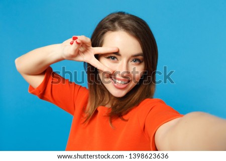 Close up photo of young woman in red orange clothes looking camera posing doing selfie shot isolated over trendy blue background, studio portrait. People lifestyle fashion concept. Mock up copy space
