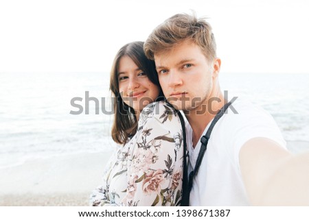 Stylish hipster couple taking selfie on beach at evening sea. Summer vacation. Portrait of happy young family on honeymoon on tropical island making selfie. Space for text