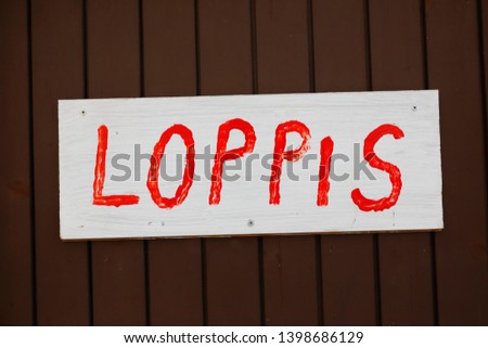White wooden sign with text in red with the Swedish word loppis for a flea market on a brown wooden wall.