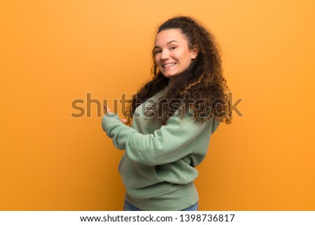 Teenager girl over ocher wall pointing back