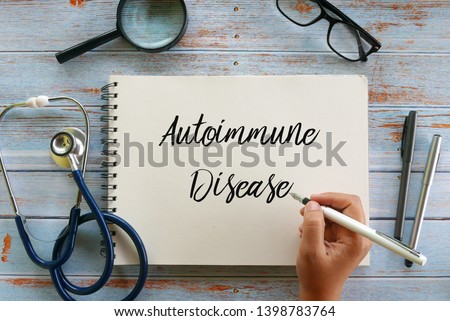 Top view of magnifying glass,glasses,stethoscope,pen and hand writing ' Autoimmune Disease ' on notebook on wooden background, Royalty-Free Stock Photo #1398783764
