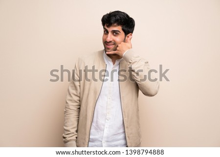 Young man over isolated wall making phone gesture. Call me back sign