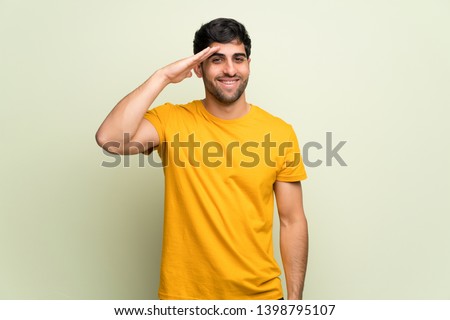 Young man over pink wall saluting with hand Royalty-Free Stock Photo #1398795107