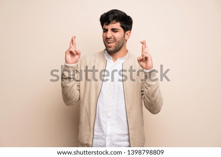 Young man over isolated wall with fingers crossing