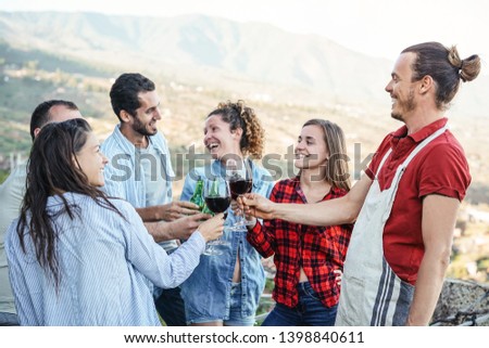 Group of happy friends cheering and toasting with red wine glasses on terrace - Young people having fun drinking at dinner party on patio with panoramic view - Friendship and youth lifestyle concept